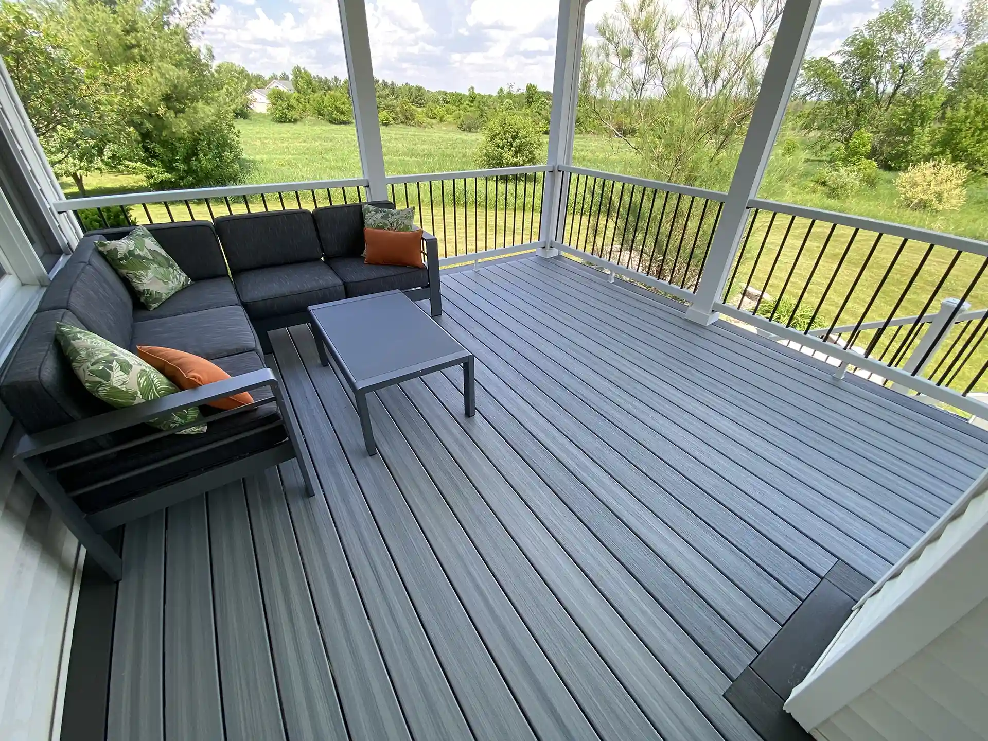 Photo of a covered deck with gray composite boards, black patio furniture, and lush green views.