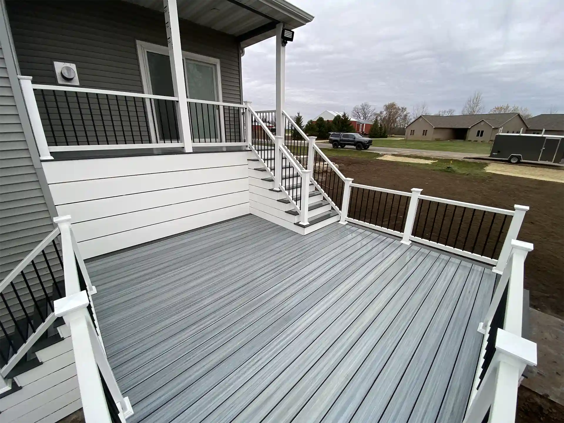 Photo of a modern gray composite deck with white and black railing, overlooking a bare lawn.